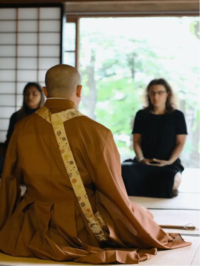 Monk and two women seated in a meditation posture inside a temple